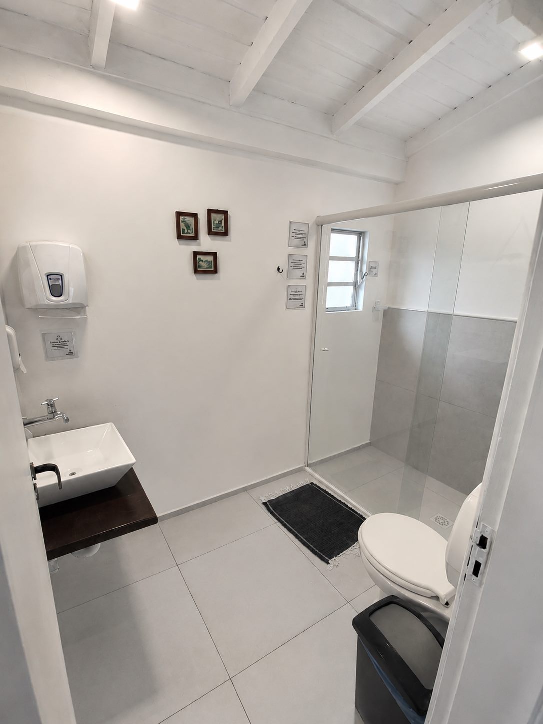 Banheiro de uso individual, claro e limpo, com box de vidro e lavatório