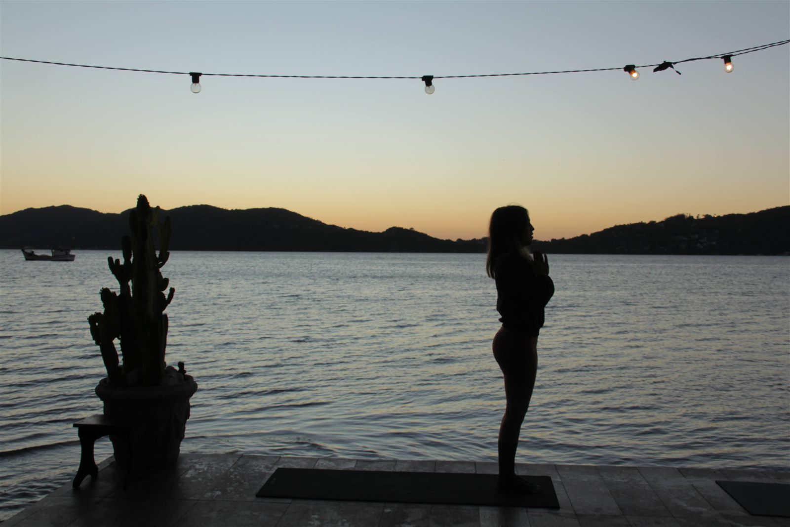 Silhueta em posição de prece no deck ao pôr do sol, à beira da lagoa